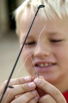 A boy placing bait on a fish hook.